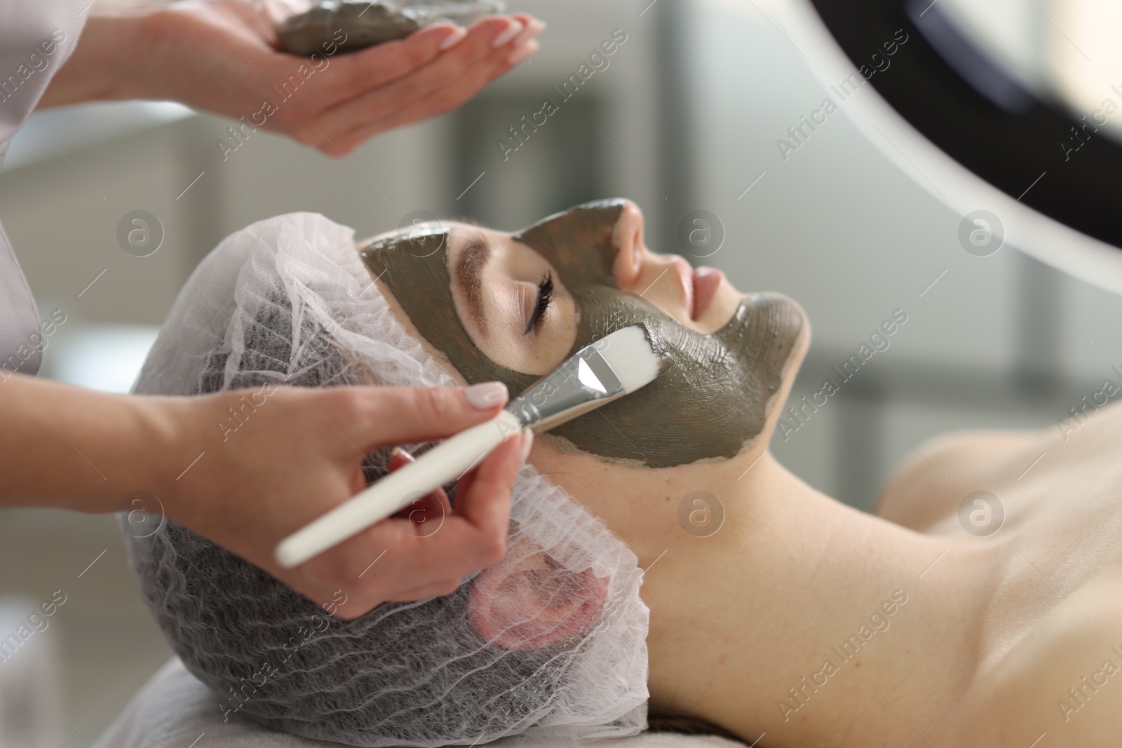 Photo of Cosmetologist applying mask on woman's face in clinic, closeup