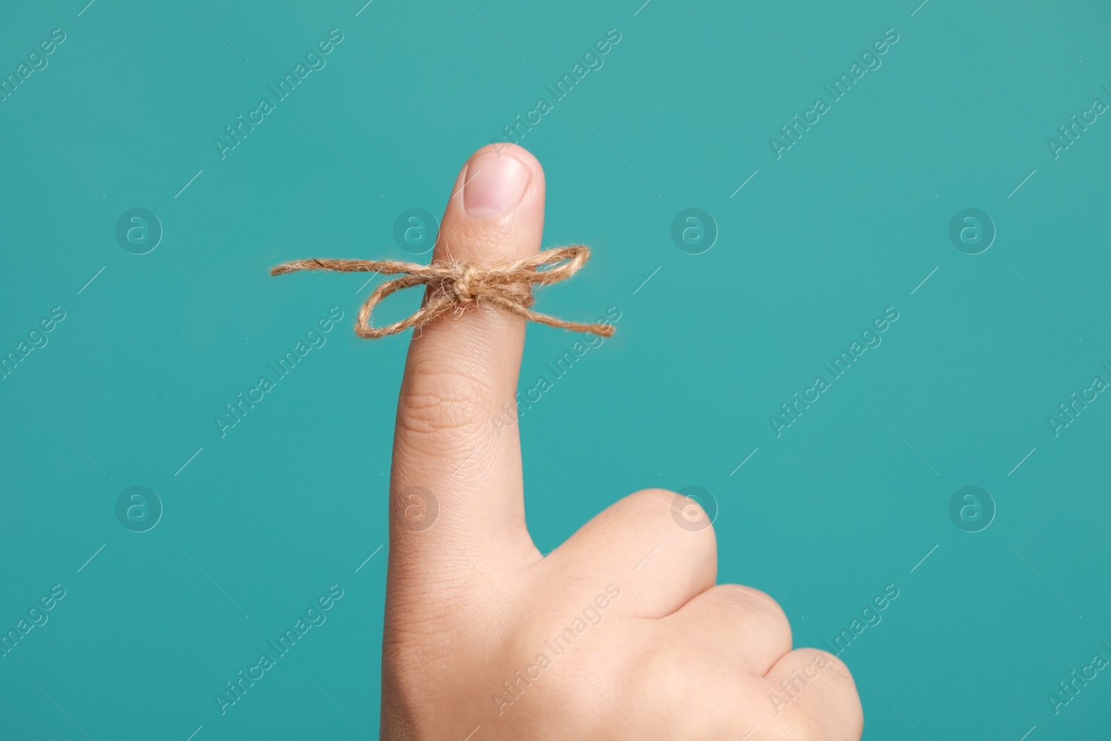 Photo of Man showing index finger with tied bow as reminder on turquoise background, closeup