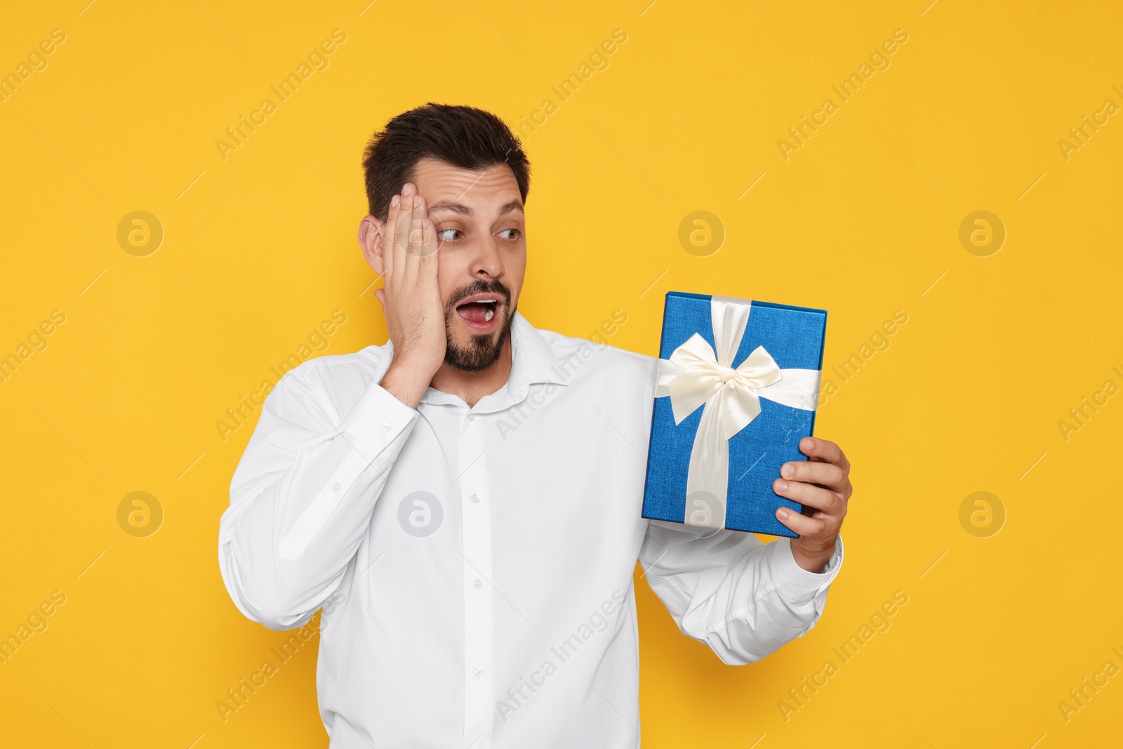 Photo of Surprised man with gift box on yellow background