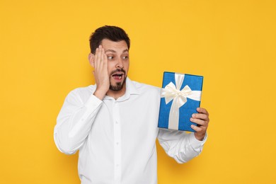 Photo of Surprised man with gift box on yellow background