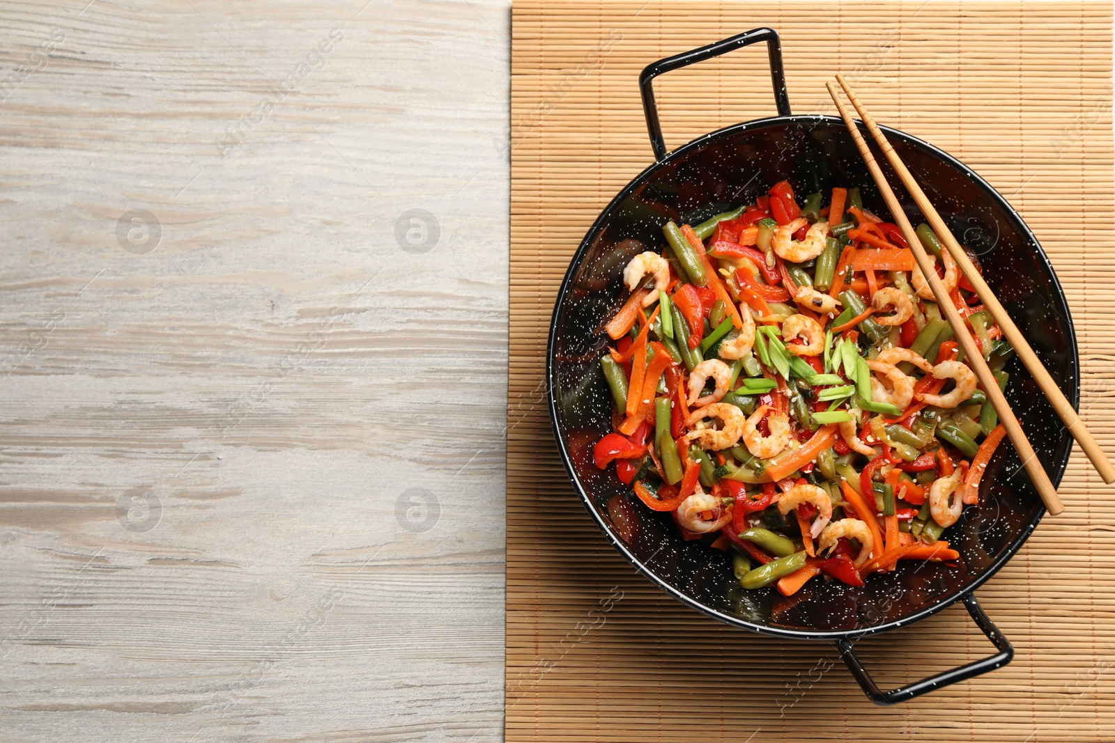 Photo of Shrimp stir fry with vegetables in wok and chopsticks on wooden table, top view. Space for text