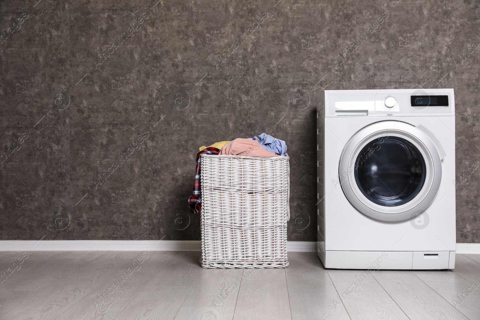 Photo of Wicker laundry basket full of dirty clothes and washing machine near color wall. Space for text