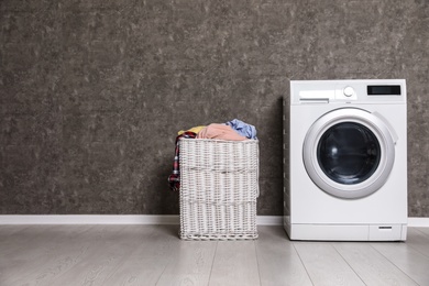 Wicker laundry basket full of dirty clothes and washing machine near color wall. Space for text