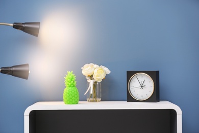 Photo of Stylish pineapple candle, flowers and clock on table against color background