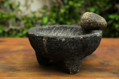 Photo of Empty stone mortar with pestle on wooden table outdoors, closeup