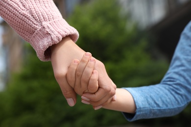 Photo of Little child holding hands with his mother outdoors, closeup. Family time