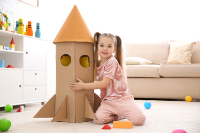 Cute little child playing with cardboard rocket at home
