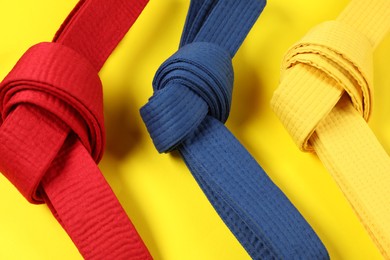 Colorful karate belts on yellow background, flat lay