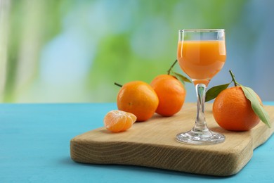 Photo of Delicious tangerine liqueur and fresh fruits on light blue wooden table, space for text