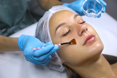 Photo of Cosmetologist applying chemical peel product on client's face in salon