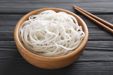 Photo of Bowl of tasty cooked rice noodles and chopsticks on black wooden table, closeup