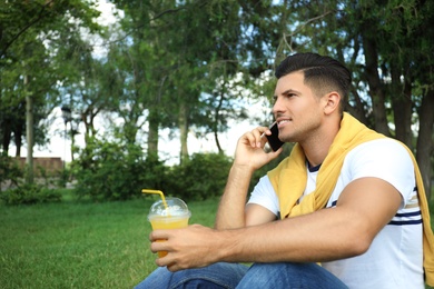 Photo of Handsome man with refreshing drink talking on smartphone in park