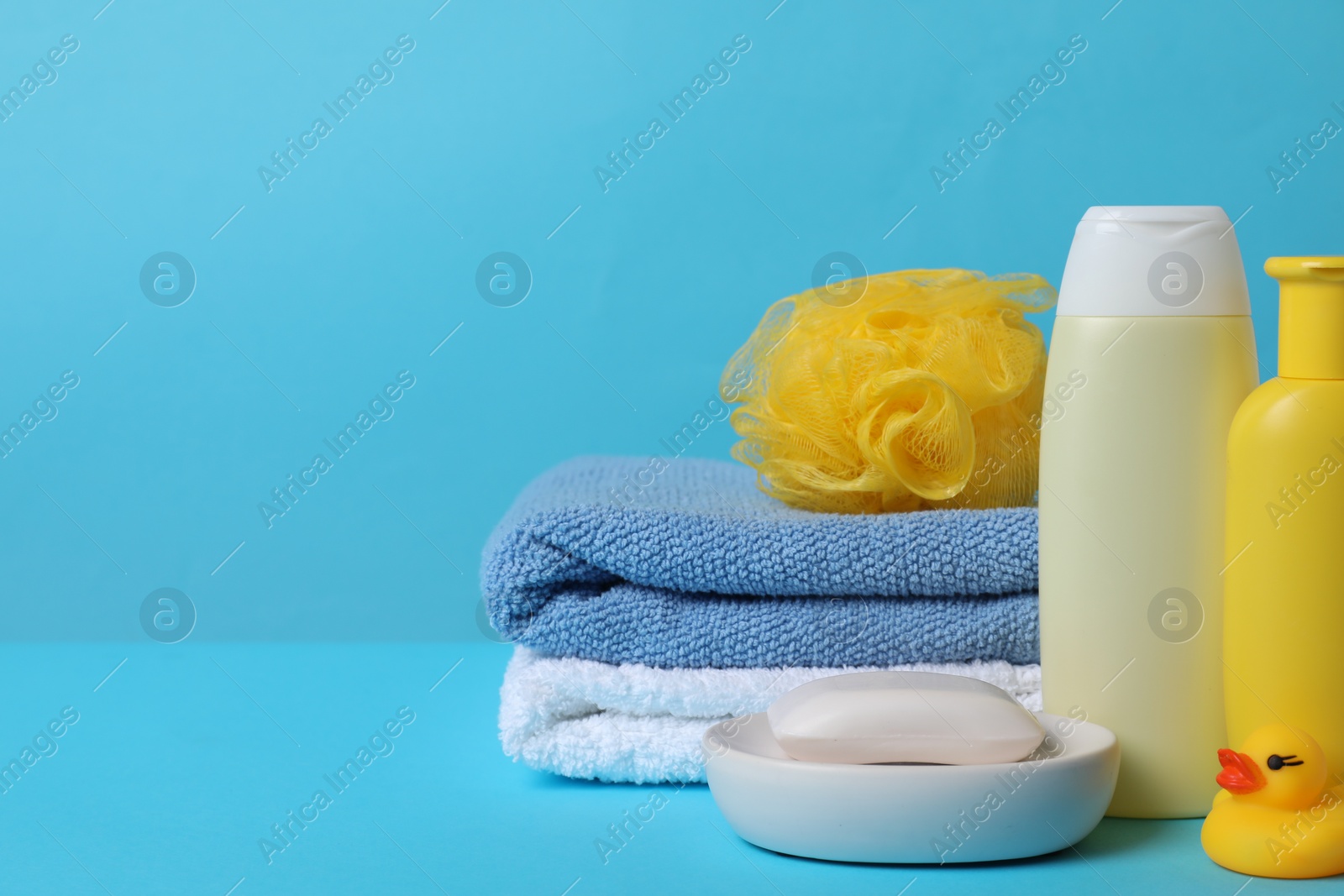 Photo of Baby cosmetic products, bath duck, sponge and towels on light blue background. Space for text