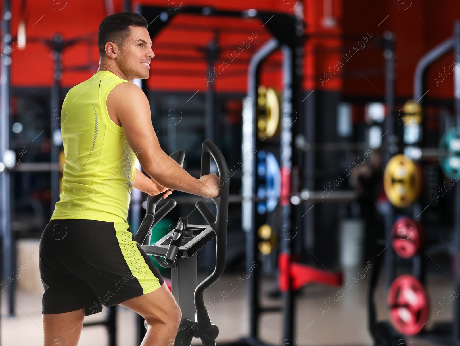 Image of Man using modern elliptical machine in gym, space for text