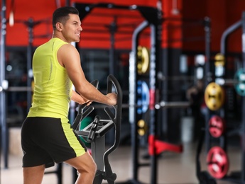 Image of Man using modern elliptical machine in gym, space for text