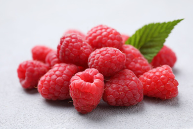 Photo of Delicious fresh ripe raspberries with green leaf on light grey table