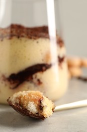 Photo of Tasty tiramisu in glass and spoon on light grey table, closeup