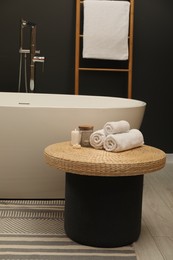 Photo of Spa day. Towels and candles on wicker table near tub in bathroom