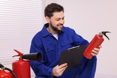 Photo of Man with clipboard checking fire extinguisher indoors