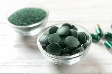 Photo of Bowls of spirulina pills and powder on wooden table, closeup