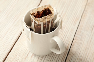 Photo of Cup with drip coffee bag on white wooden table, closeup