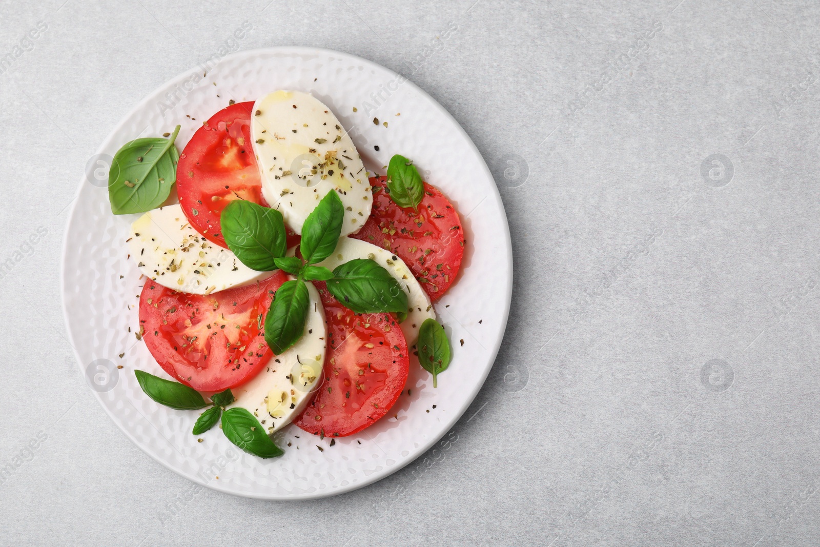 Photo of Plate of delicious Caprese salad with herbs on light grey table, top view. Space for text