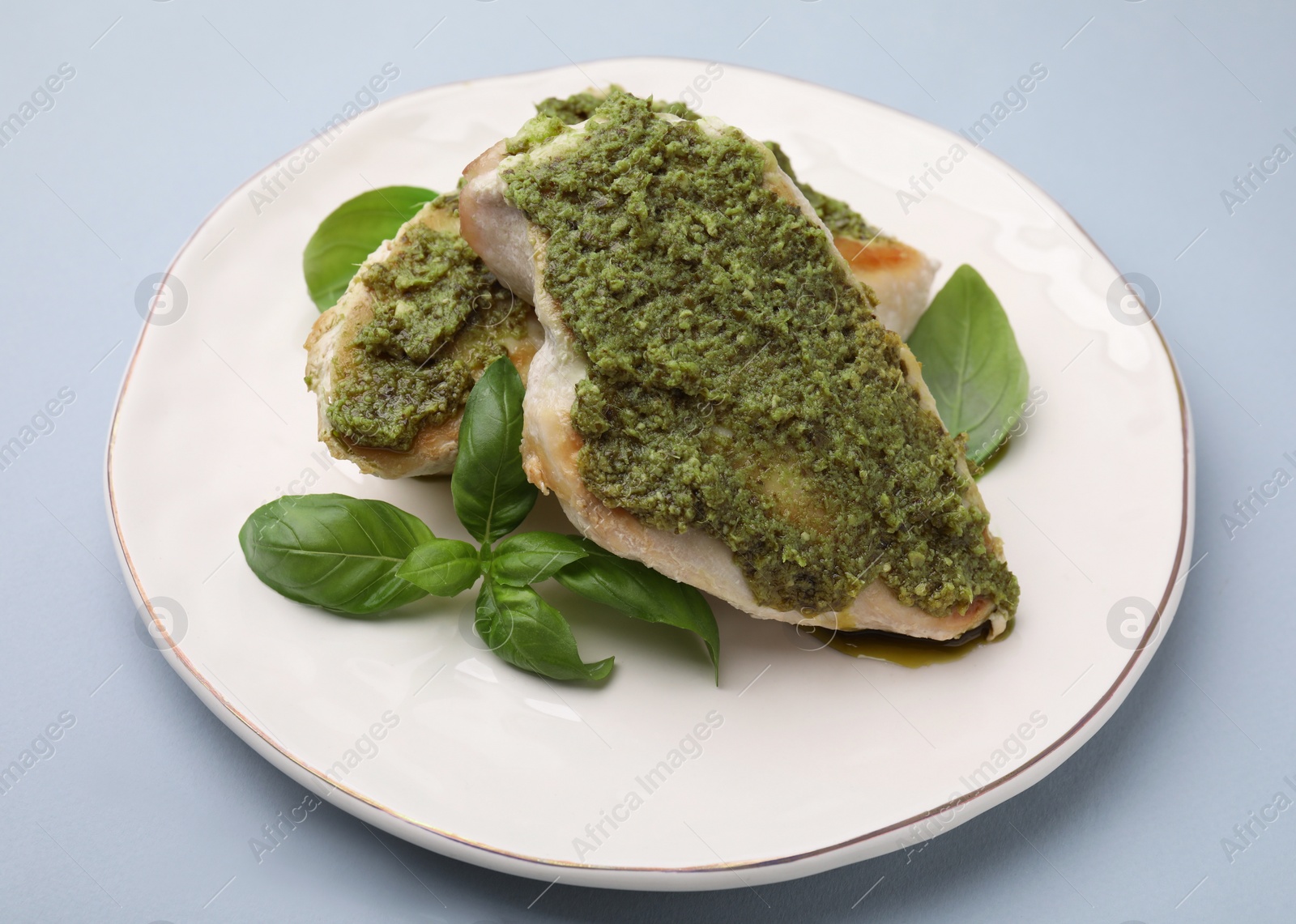 Photo of Delicious chicken breasts with pesto sauce and basil on light gray table, closeup