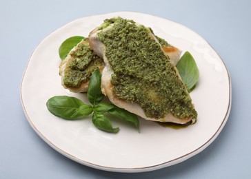 Delicious chicken breasts with pesto sauce and basil on light gray table, closeup