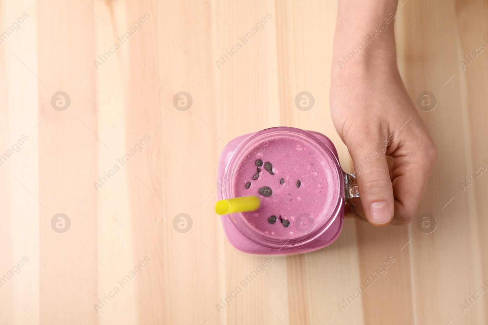 Photo of Woman with tasty milk shake at wooden table, top view. Space for text