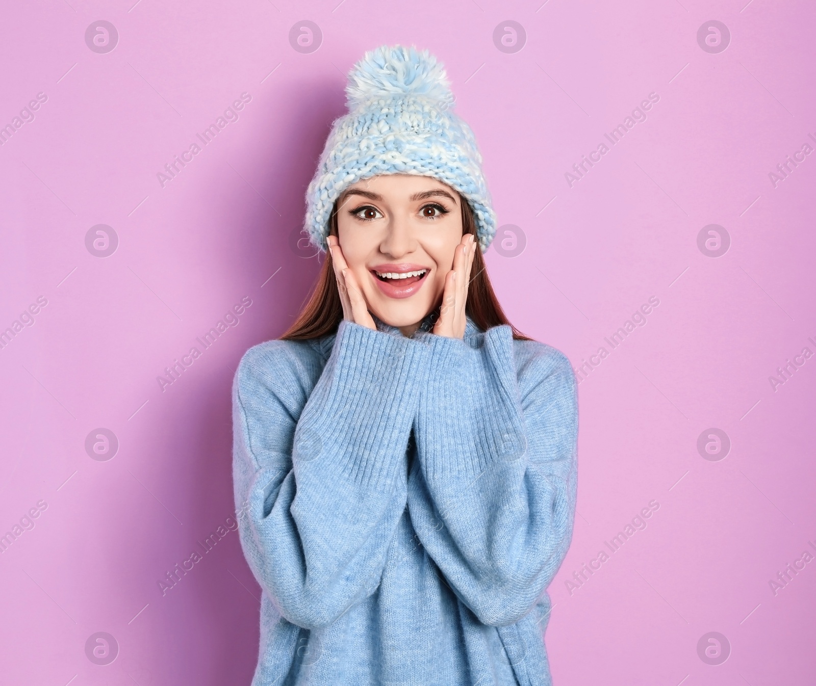 Photo of Emotional woman wearing warm sweater and hat on pink background. Winter season