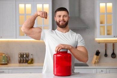 Young man with jar of protein powder at white marble table in kitchen