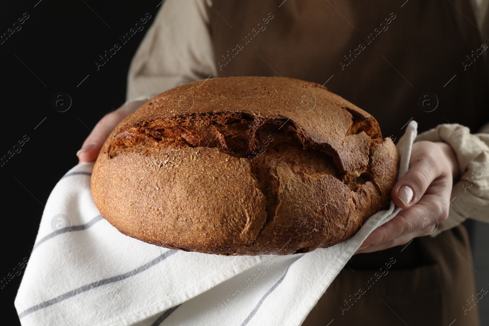 Photo of Woman holding freshly baked bread on black background, closeup