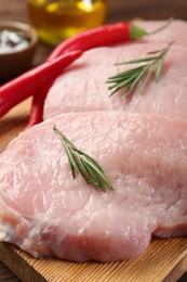 Photo of Pieces of raw pork meat, rosemary and chili peppers on board, closeup