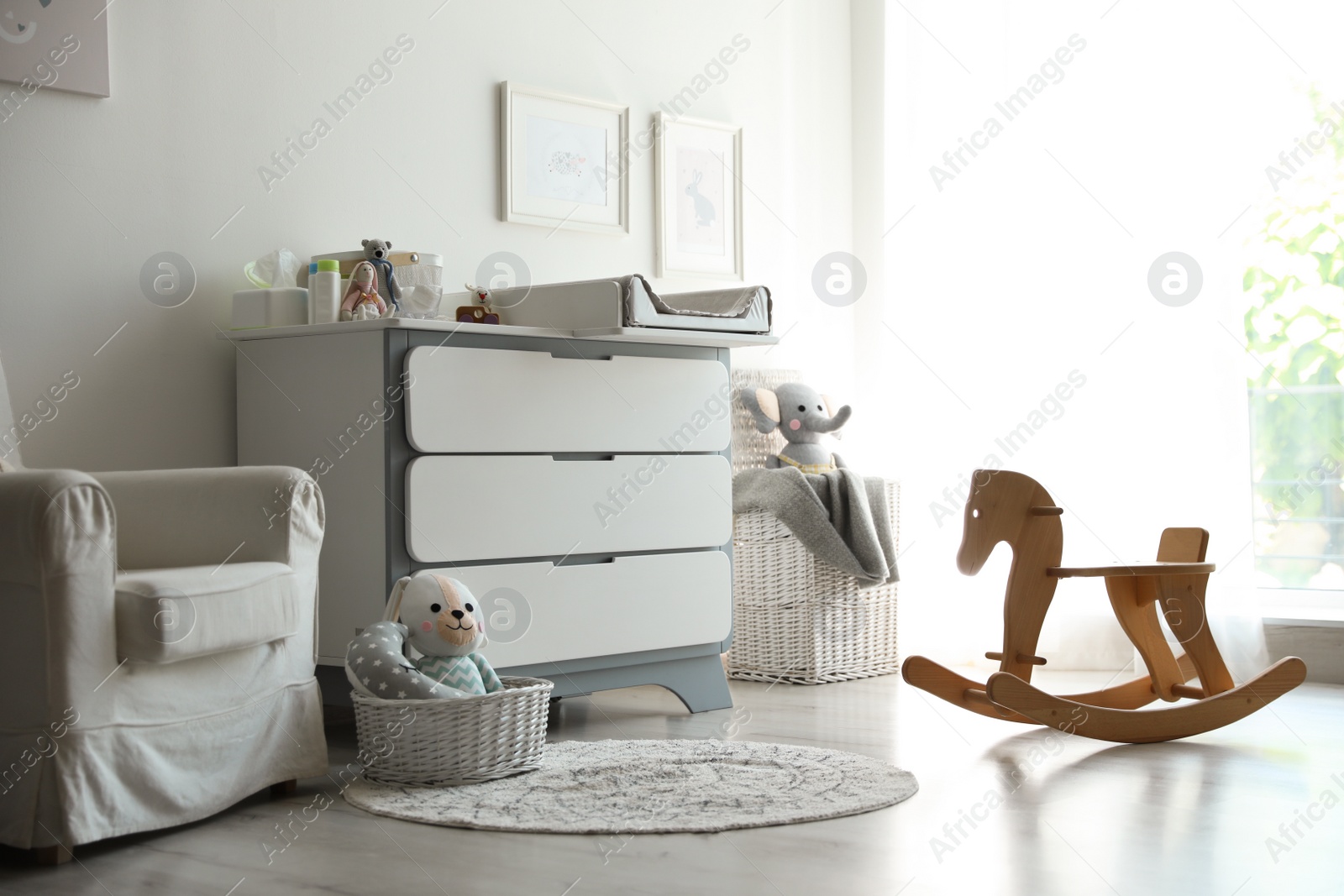 Photo of Beautiful baby room interior with toys, armchair and modern changing table