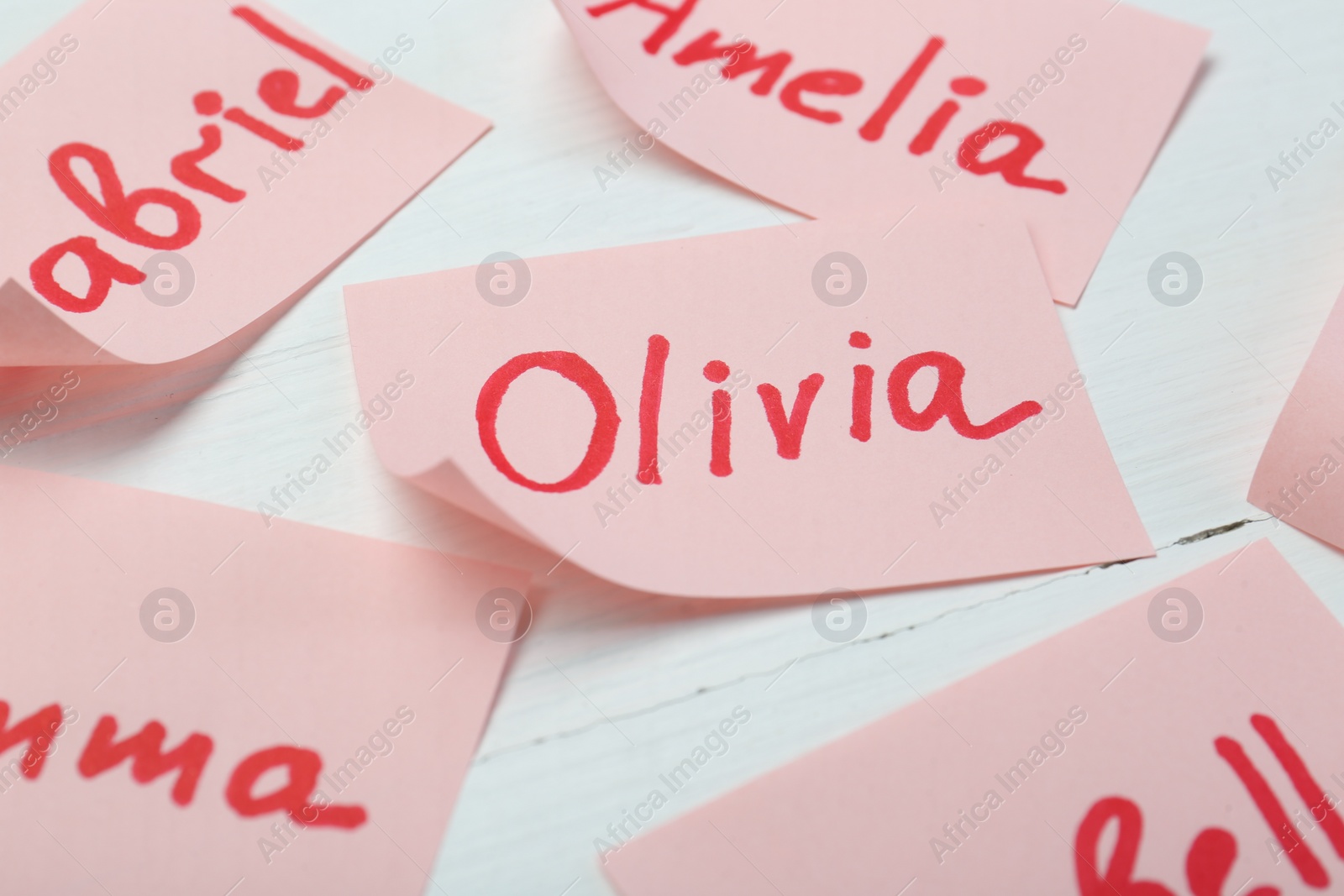 Photo of Paper stickers with different names on white wooden table, closeup. Choosing baby's name