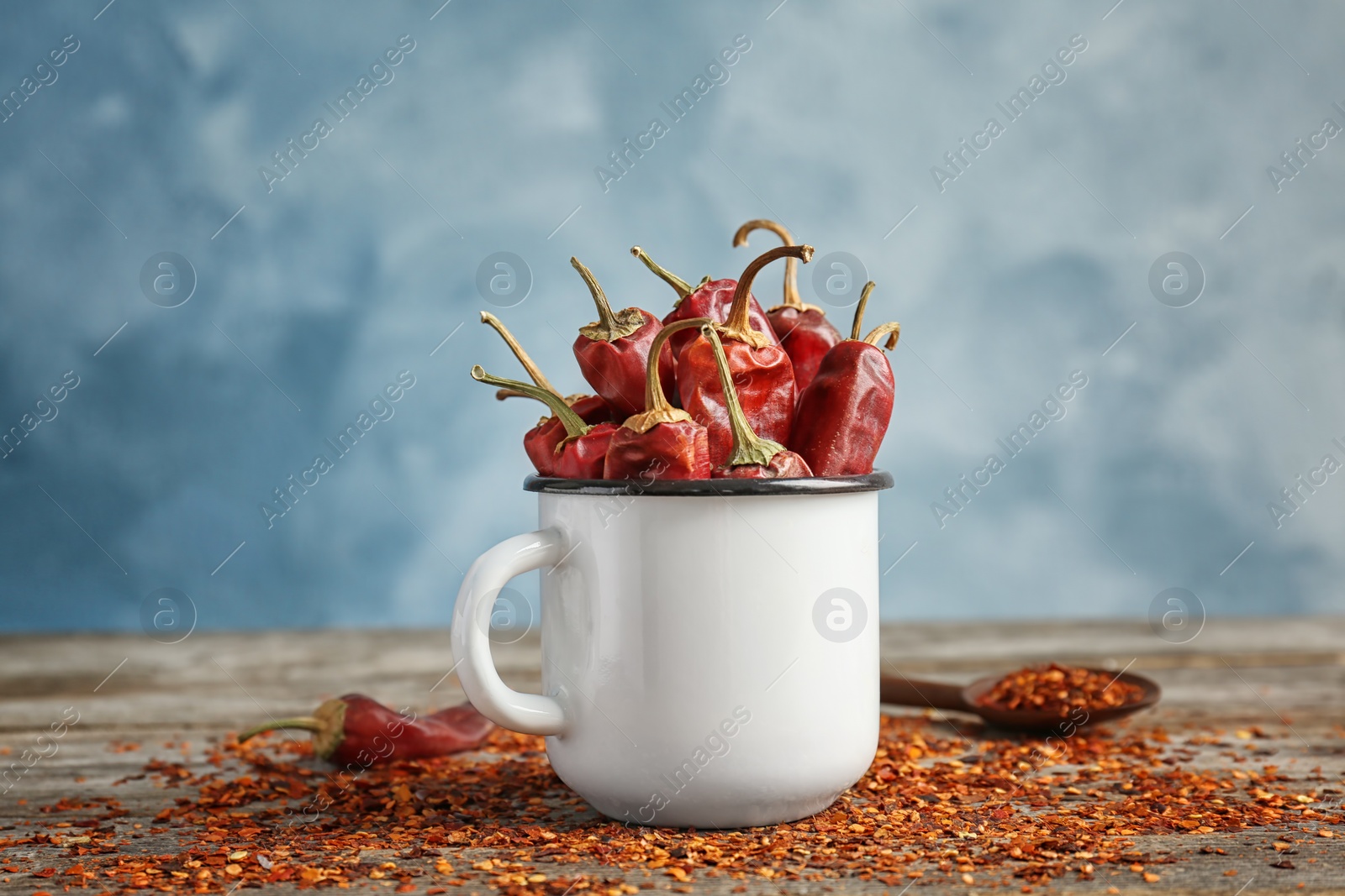 Photo of Mug with dry chili peppers and powder on wooden table