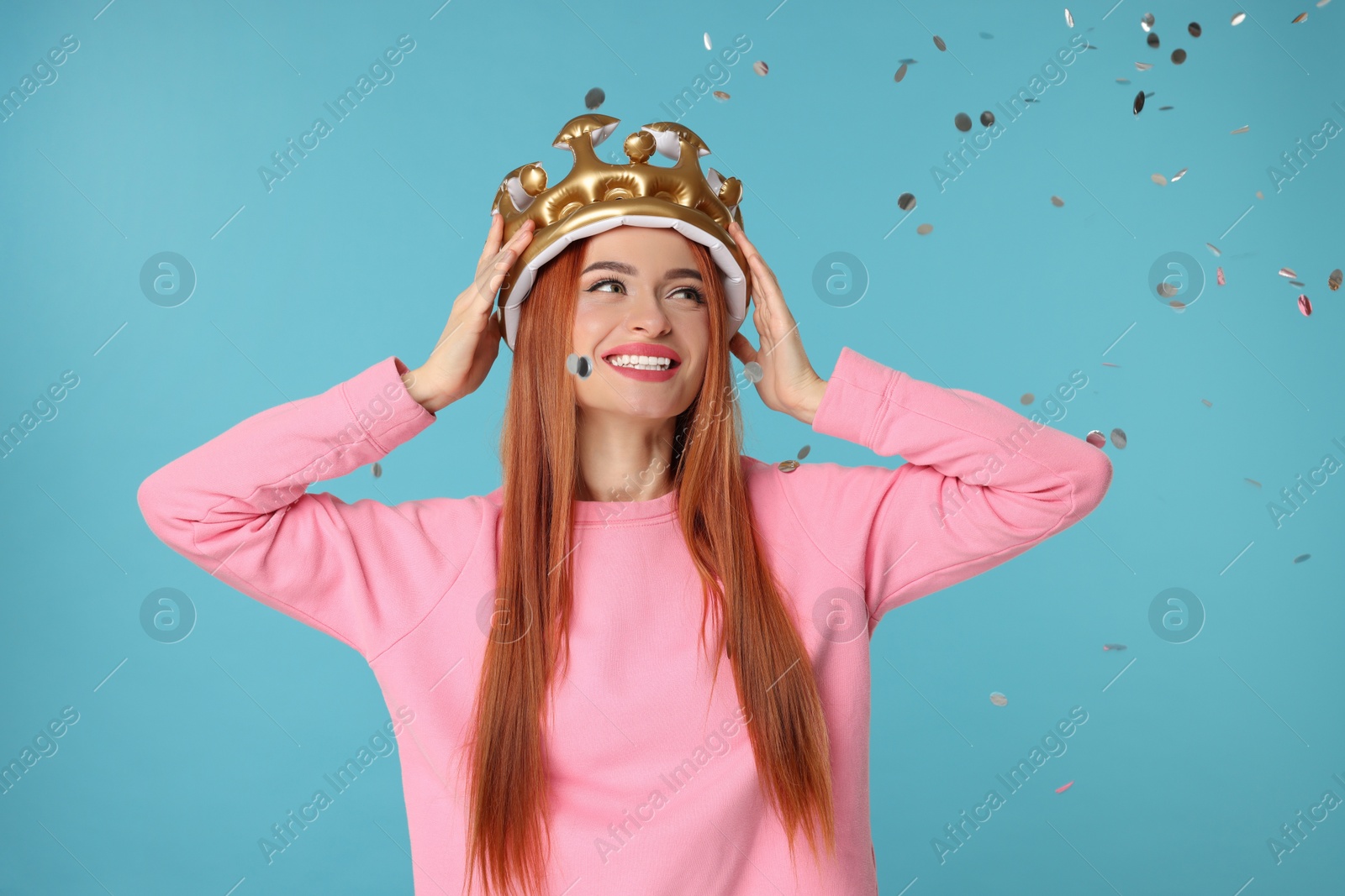 Photo of Beautiful young woman with inflatable crown under falling confetti on light blue background