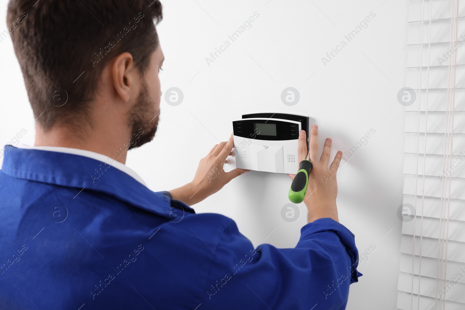 Photo of Technician installing home security alarm system on white wall indoors