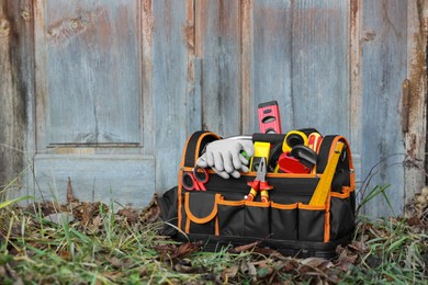 Photo of Bag with different tools for repair on grass near wooden door outdoors, space for text