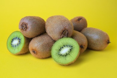 Heap of whole and cut fresh kiwis on yellow background