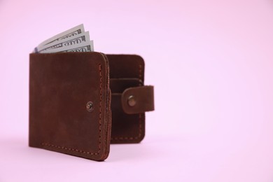 Stylish brown leather wallet with dollar banknotes on pink background, space for text