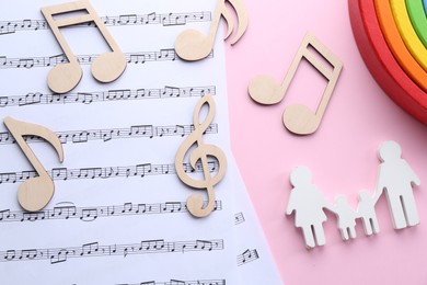 Baby songs. Music sheets, figures of family, wooden notes and toy rainbow on pink background, flat lay