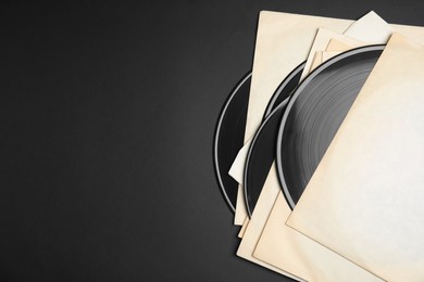 Photo of Vintage vinyl records in paper sleeves on black background, flat lay. Space for text