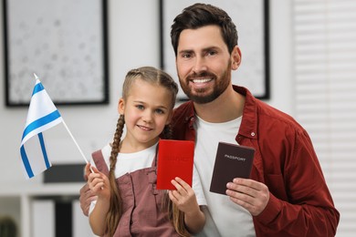 Immigration. Happy man with his daughter holding passports and flag of Israel indoors