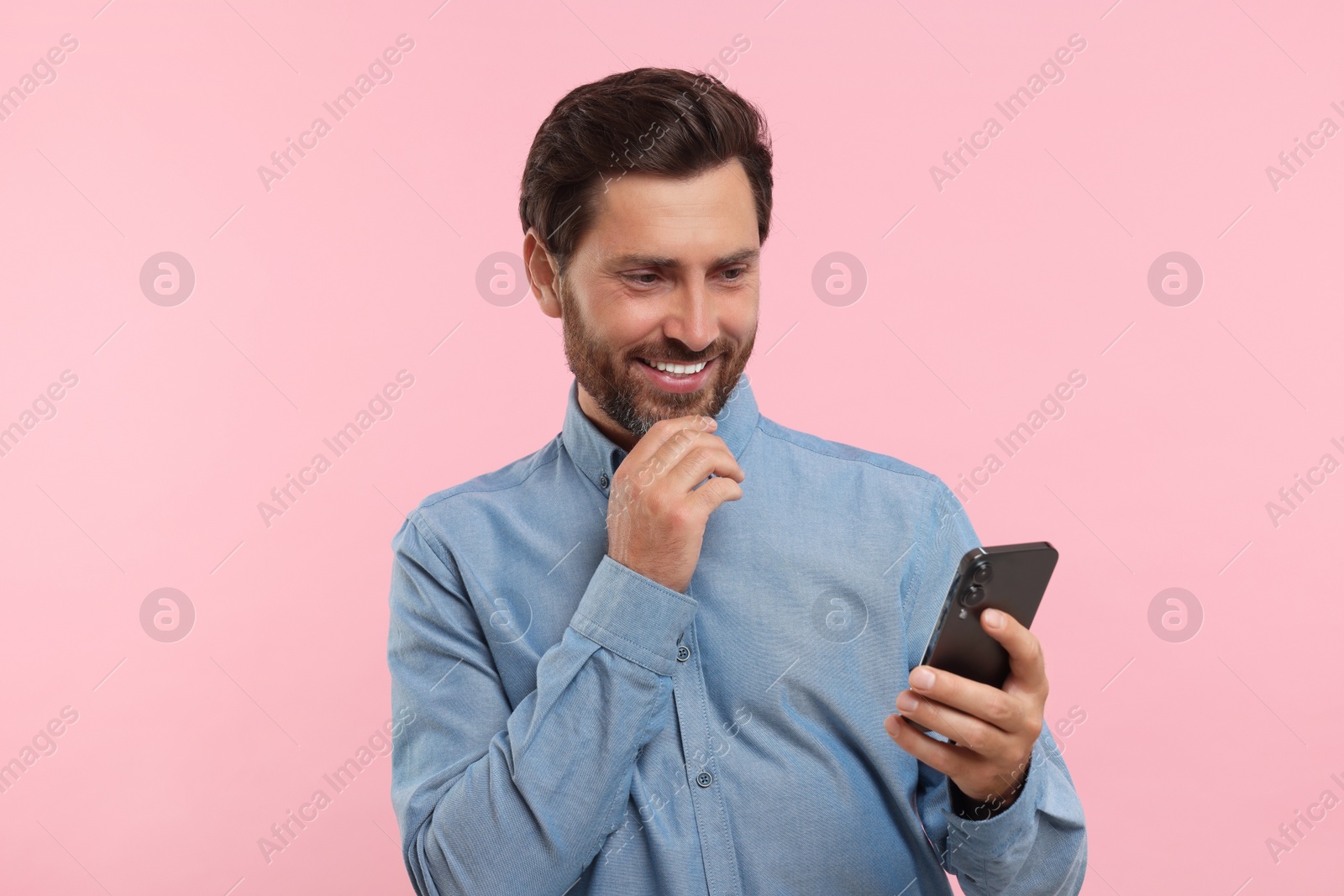 Photo of Handsome bearded man using smartphone on pink background