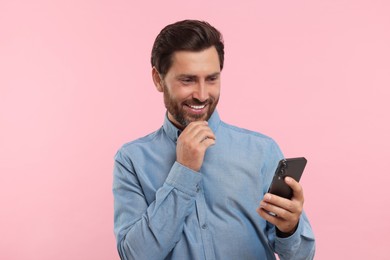 Photo of Handsome bearded man using smartphone on pink background