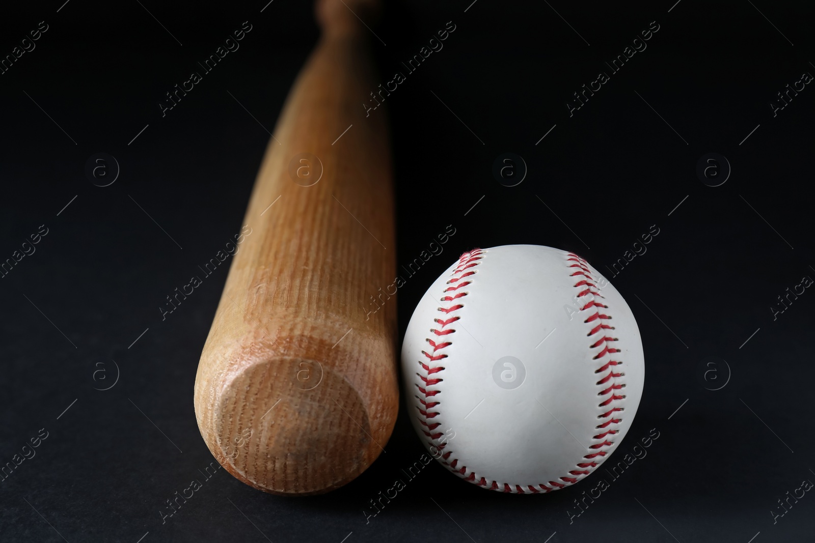 Photo of Wooden baseball bat and ball on black background, closeup. Sports equipment