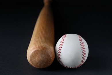 Photo of Wooden baseball bat and ball on black background, closeup. Sports equipment