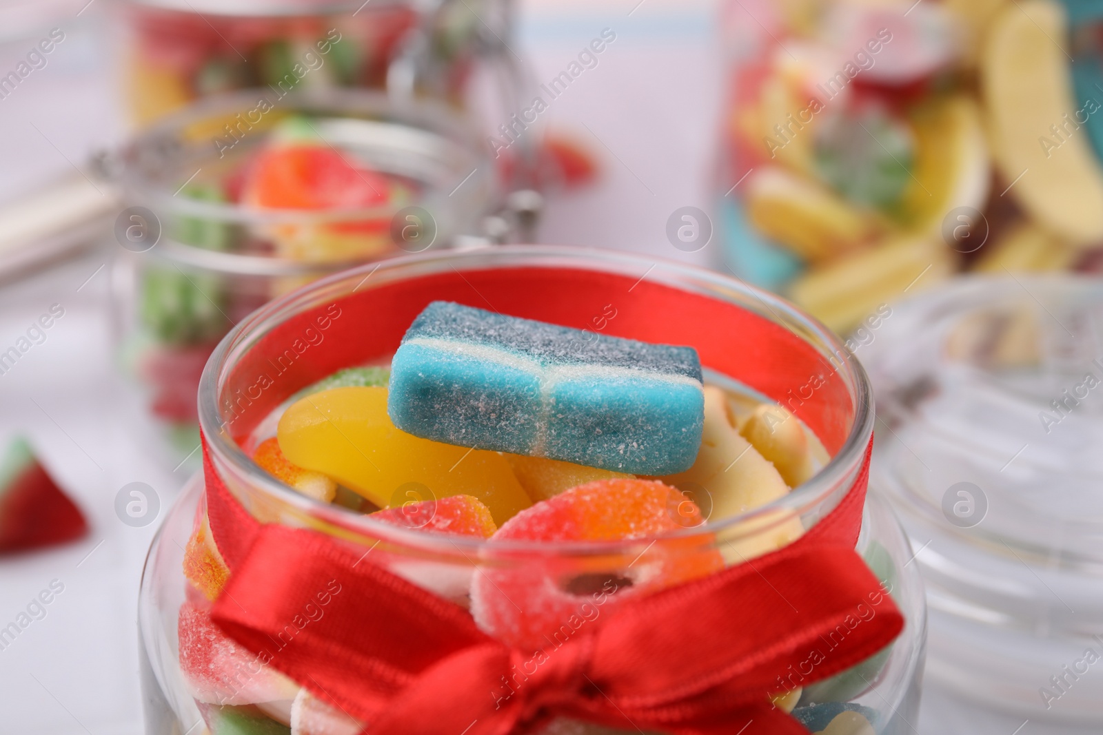 Photo of Glass jar with tasty colorful jelly candies on table, closeup