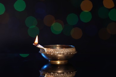 Photo of Lit diya on dark background with blurred lights, space for text. Diwali lamp